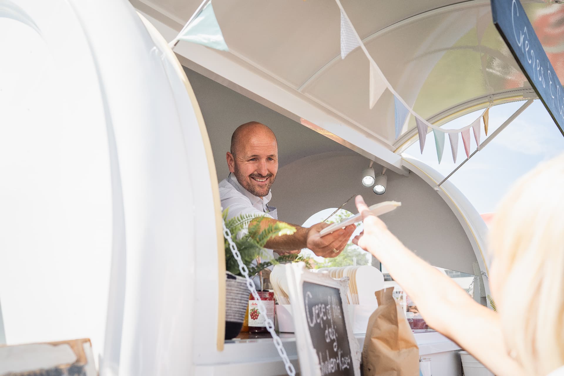 Freundliche Übergabe eines frischen Crêpes am Fenster des Trailers